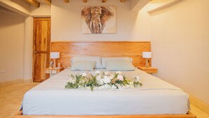 A bedroom with a wooden bed, two bedside tables with lamps, a floral arrangement on the bed, and a wooden door. - Anaho Beach Club (Cartagena)