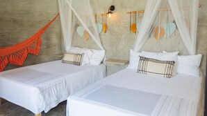 Two single beds with white bedding and a mosquito net, a small orange hammock, and wall-mounted decorative items. - Casa con Habitación Doble, Casa Maya (Izamal)