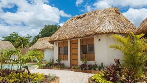 A bungalow with a thatched roof, surrounded by tropical plants and a clear sky. - Casa con Habitación Doble, Casa Maya (Izamal)