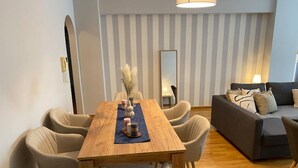 A modern living room with a wooden dining table, beige chairs, a grey sofa, and a mirror on the wall. - Classy 3BR with 2 Bathrooms Apartment in Marousi (Athens)