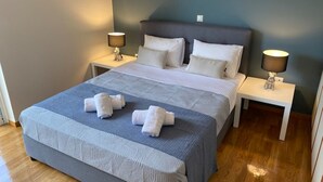 A neatly made bed with a grey and white patterned bedspread, two white pillows, and two bedside lamps on matching nightstands. - Classy 3BR with 2 Bathrooms Apartment in Marousi (Athens)