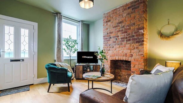 A living room with a brick fireplace, a television, a green armchair, and a brown sofa. - NEW! Stylish home, amazing location, sleeps 6! (Chester)