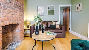 A living room with a brick fireplace, a brown leather sofa, a round wooden coffee table, and a green ottoman. - NEW! Stylish home, amazing location, sleeps 6! (Chester)