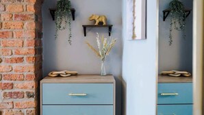 A room with a brick wall, a blue dresser with gold handles, a small shelf with a golden elephant figurine, and two hanging plants. - NEW! Stylish home, amazing location, sleeps 6! (Chester)