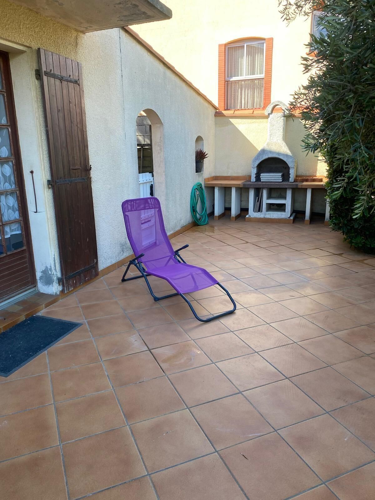 A patio with a purple chair, a grill, and a door with a window.