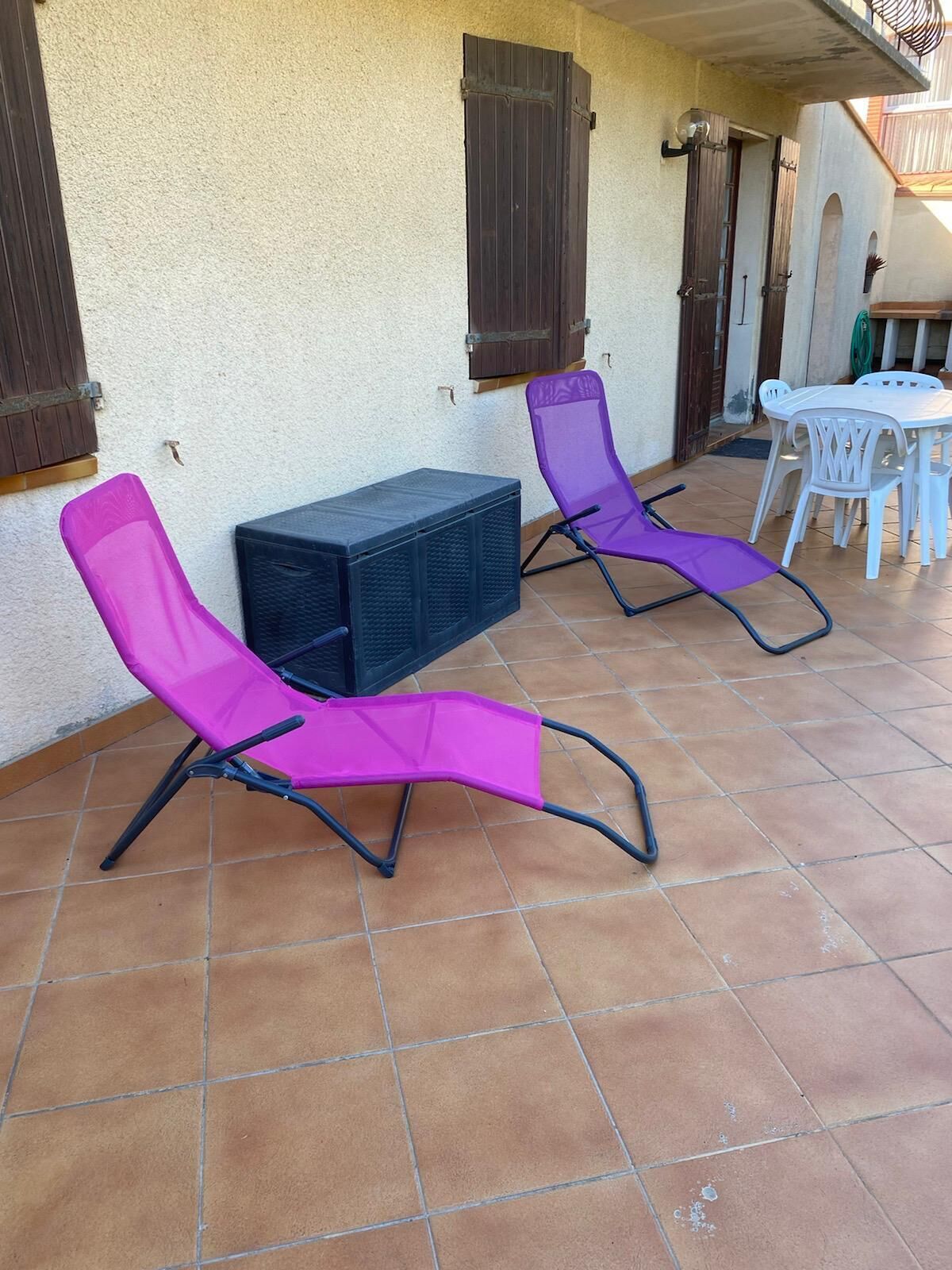 Dos sillones morados y una pequeña mesa en un patio con baldosas.