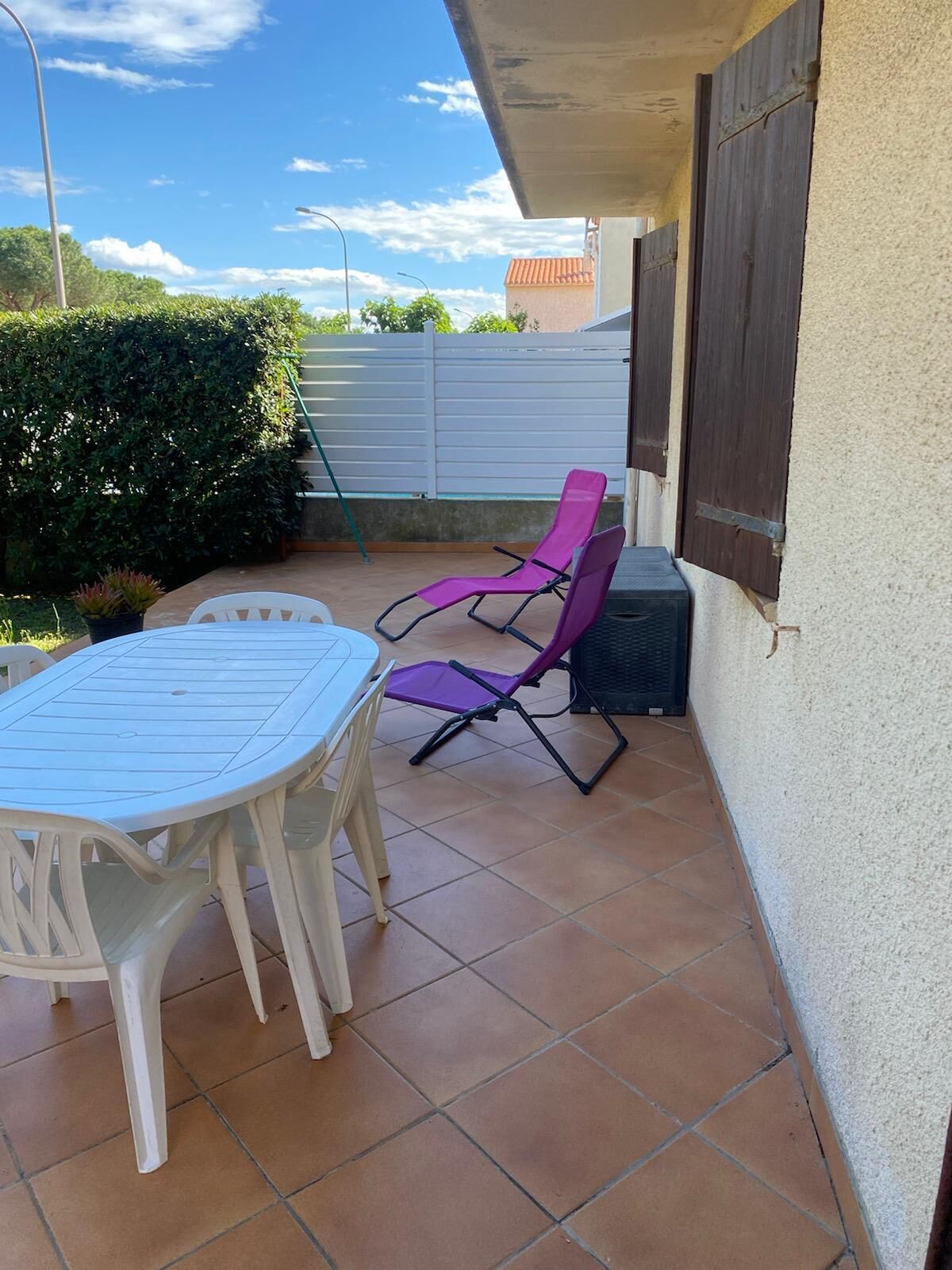An outdoor patio with a white table and two purple chairs.