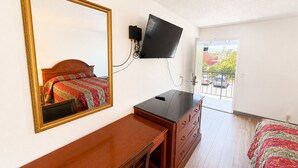 Une chambre à coucher comprenant un lit, une commode, un téléviseur fixé au mur et une porte donnant sur un balcon.
