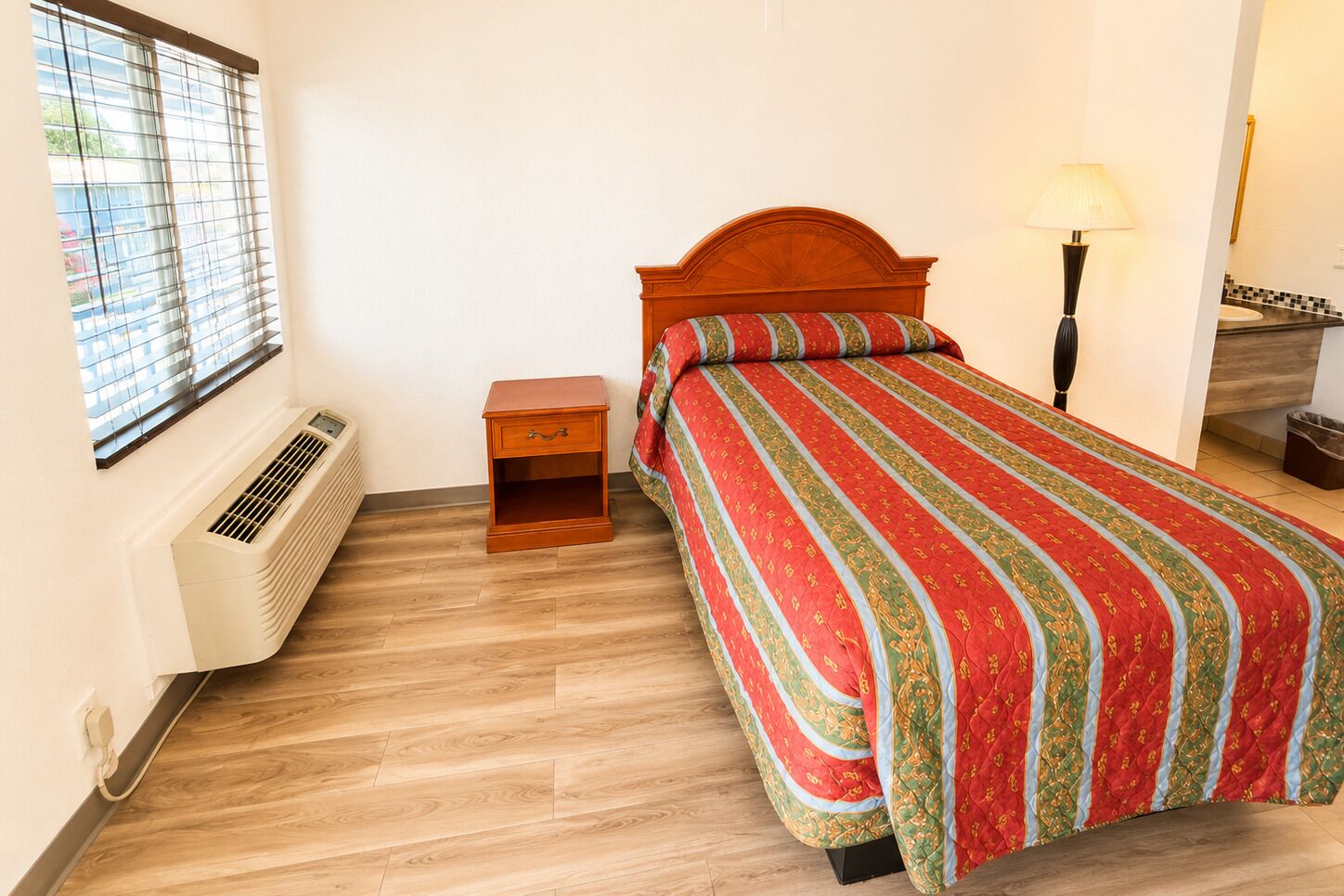 A bedroom with a bed, bedside table, lamp, and air conditioning unit.