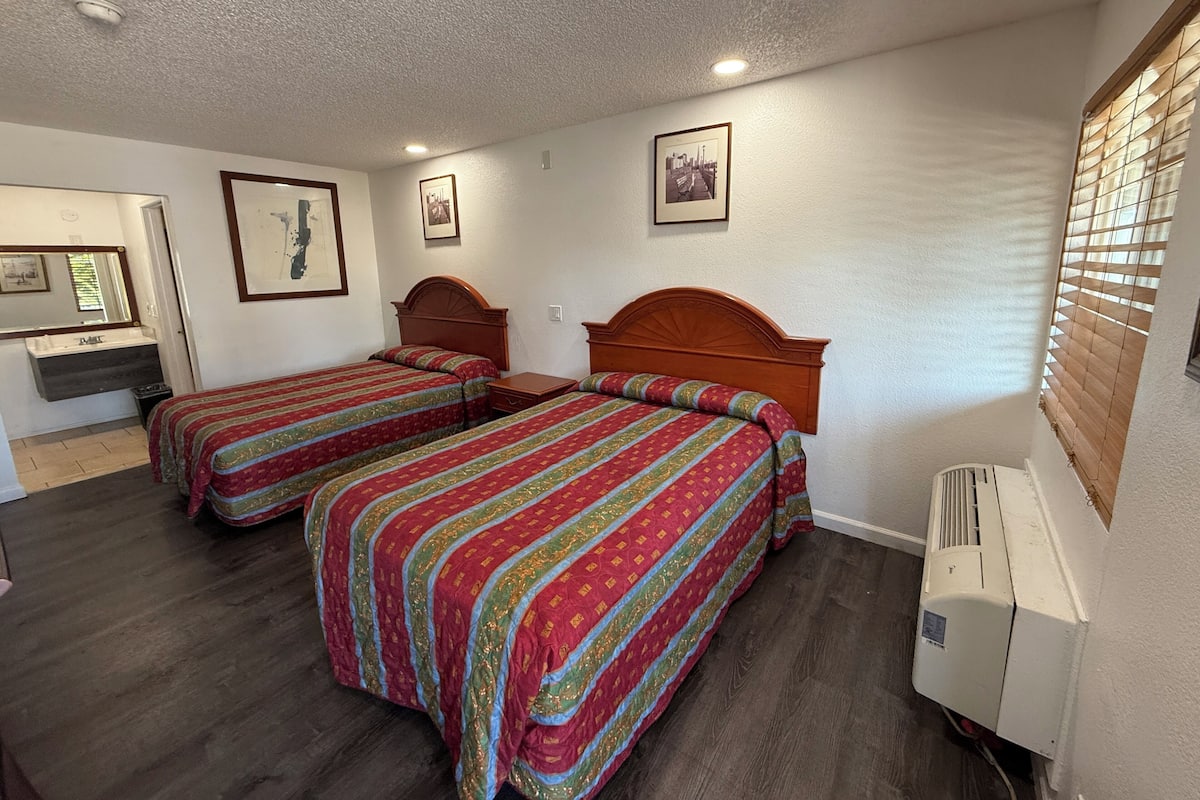 Une chambre avec deux lits, une salle de bain et une fenêtre avec des stores.