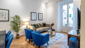 A modern living room with a sofa, two blue armchairs, a coffee table, a TV, and a large window with curtains. - Genteel Home Giraldi (Florence)