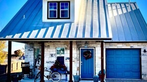 Ein Haus mit einem Metall-Dach, einer Steinterrasse, einer blauen Tür und einer Garage.