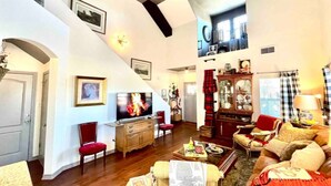 Ein geräumiges Wohnzimmer mit hoher Decke, einem Fernseher, einem Kamin und einer Treppe, die in eine obere Etage führt.
