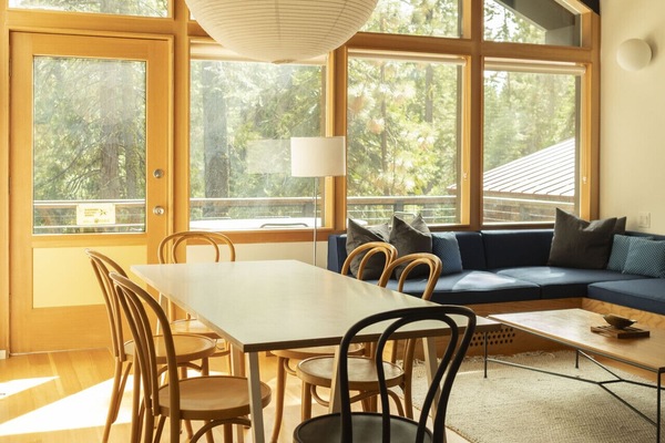 Open concept living room with custom built-in sectional sofa, large dining table, gas fireplace and large windows allowing for lots of natural light.