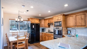 A modern kitchen with wooden cabinets, a granite countertop, a built-in oven, and a dining area with a table and chairs. - Cozy Comfy Condo MH107| Near Powder Mtn | Hot Tub (Eden)