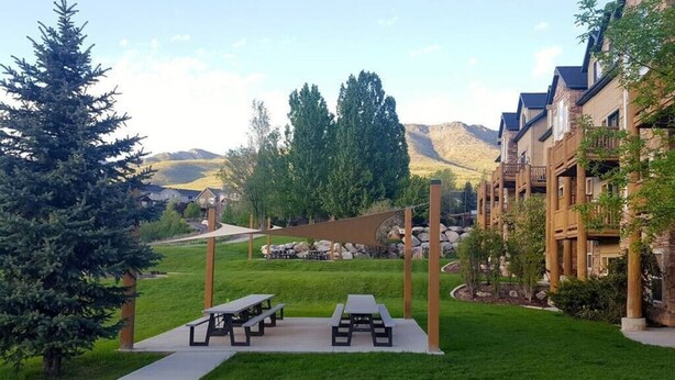 A courtyard with picnic tables, a shaded area, and a view of mountains in the background. - Cozy Comfy Condo MH107| Near Powder Mtn | Hot Tub (Eden)