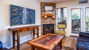 A living room with a fireplace, a large painting, a wooden table, and a couch. - Cozy Comfy Condo MH107| Near Powder Mtn | Hot Tub (Eden)