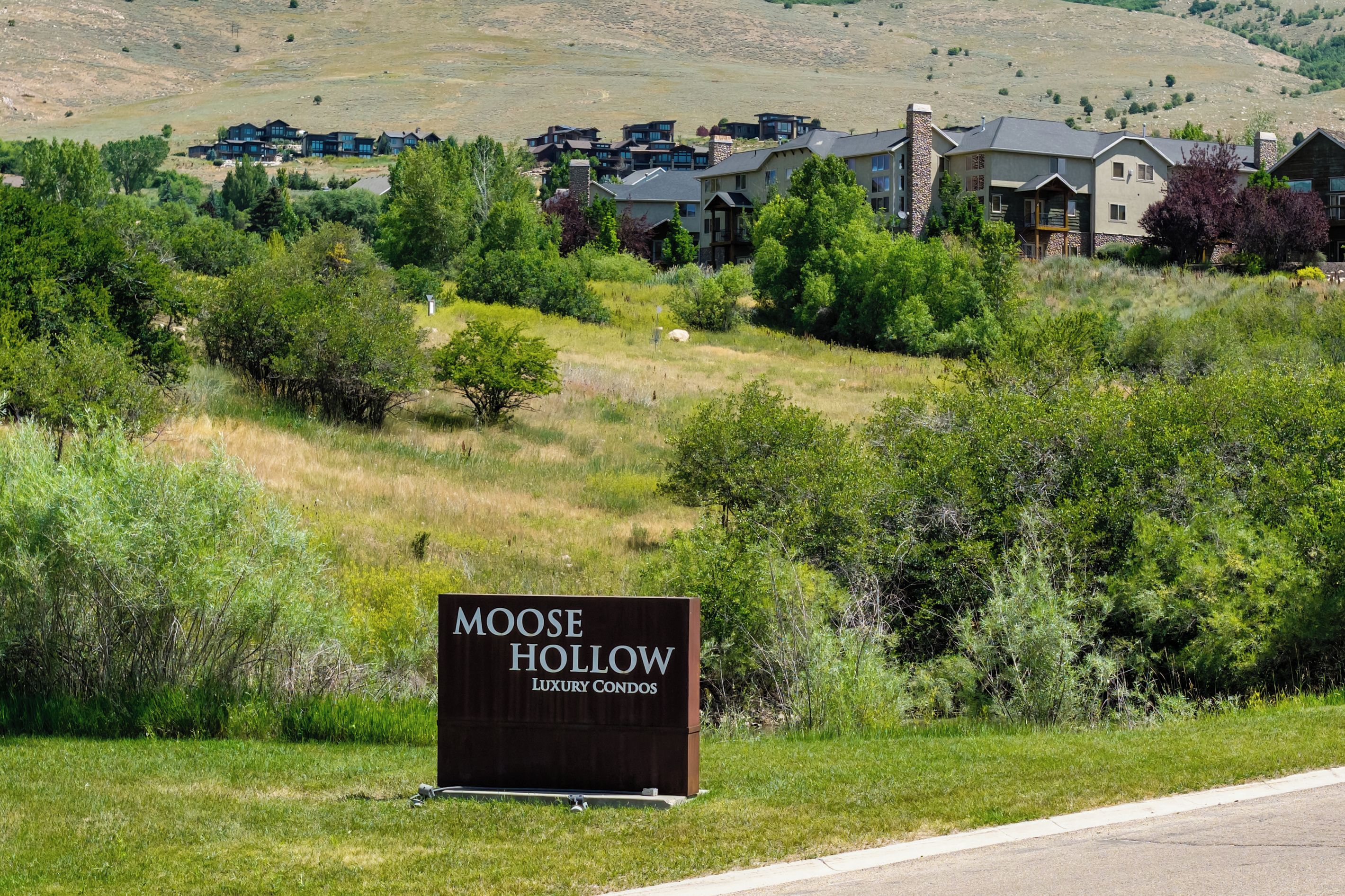 A sign for Moose Hollow Luxury Condos with a view of modern buildings and a hilly landscape.