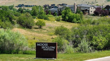 A sign for Moose Hollow Luxury Condos with a view of modern buildings and a hilly landscape.