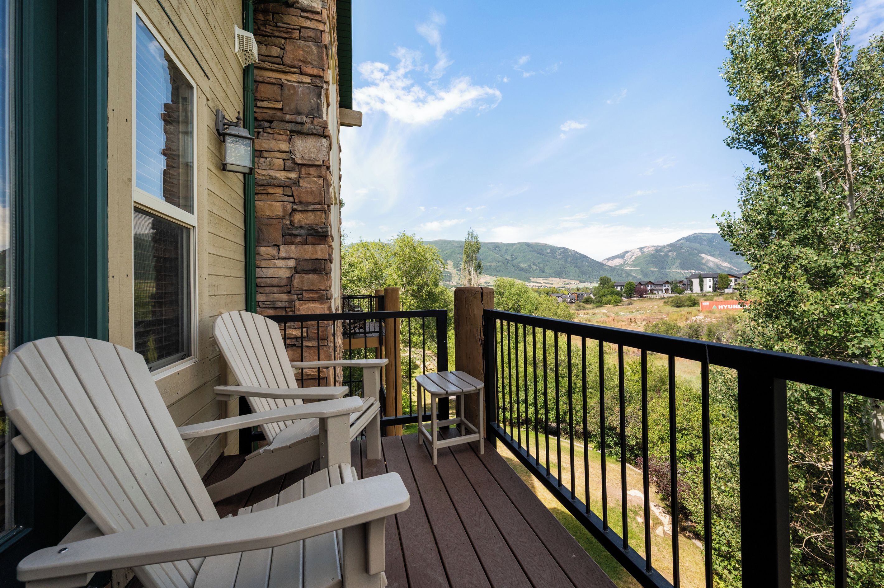A wooden deck with Adirondack chairs and a small table, overlooking a mountainous landscape.