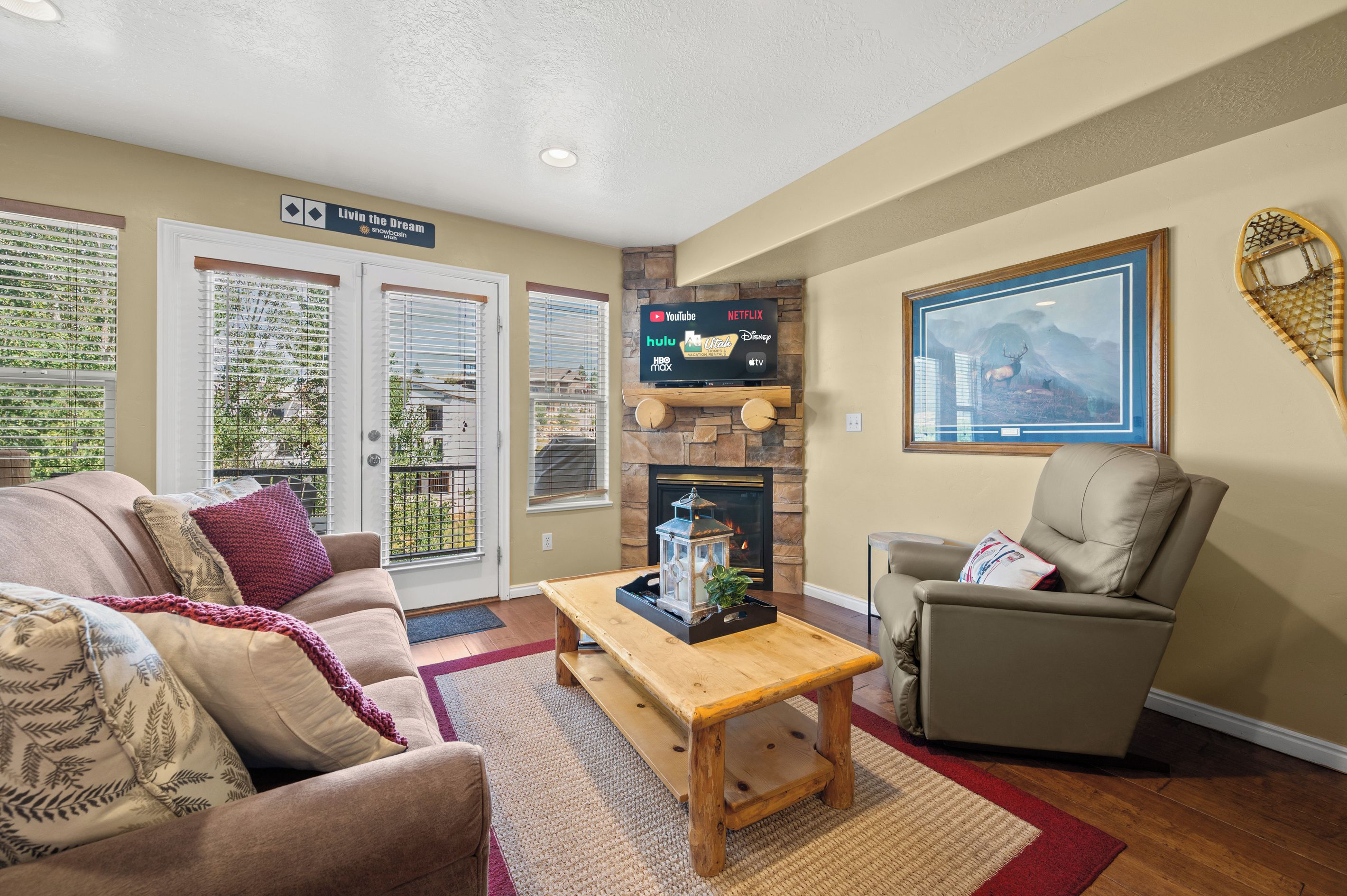 A living room with a fireplace, a television mounted on a stone wall, and a large framed picture of a mountain scene.