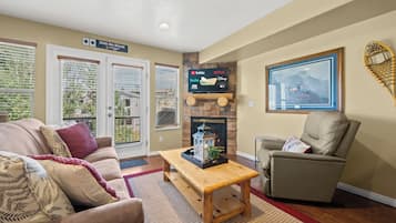 A living room with a fireplace, a television mounted on a stone wall, and a large framed picture of a mountain scene.
