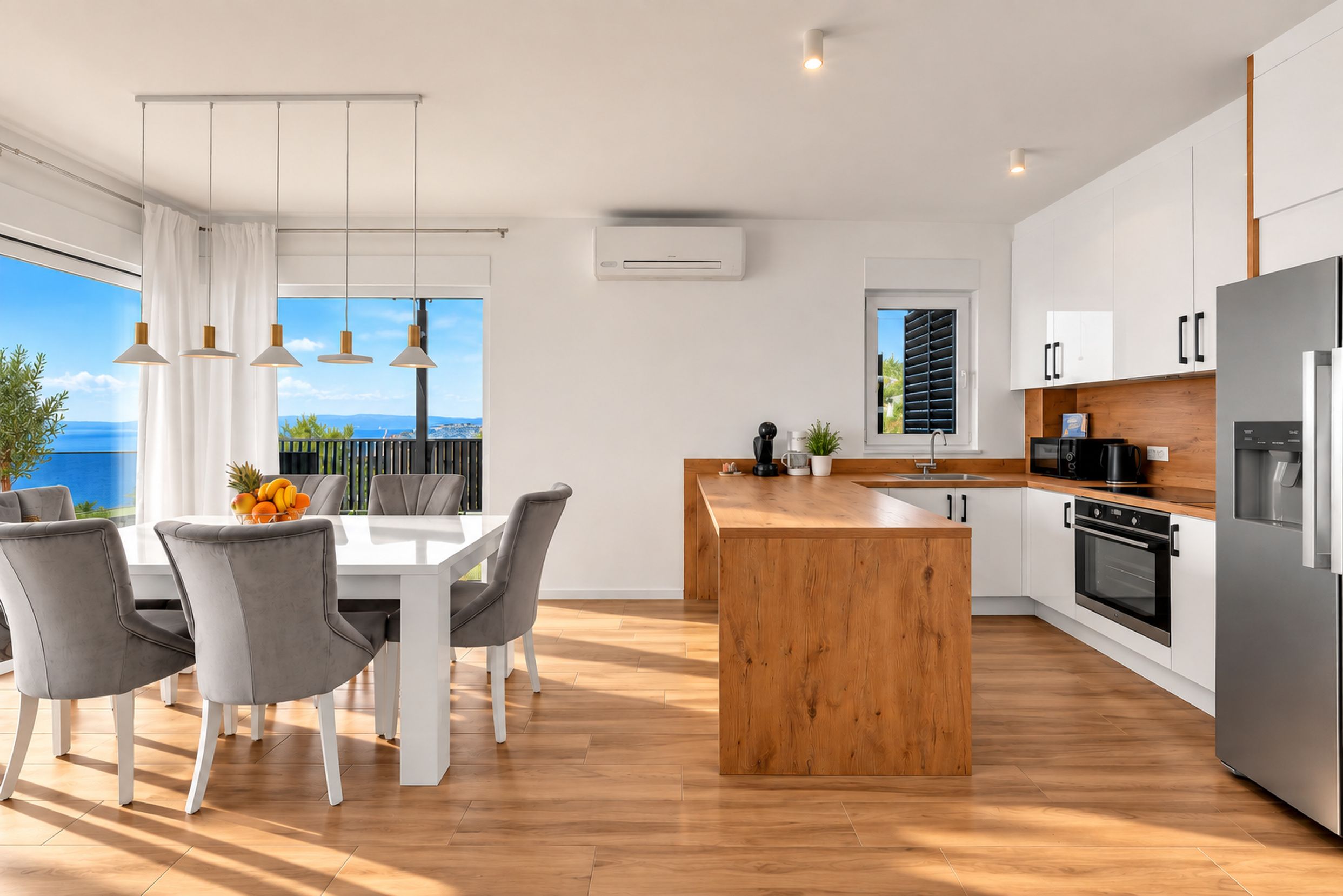 A modern kitchen with a wooden island, white cabinetry, and a view of the sea.