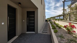 A modern building with two black doors, a paved walkway, and a garden with red flowers. - Villa VIP with heaed swimming pool and 4 Bedrooms, Several terraces with seaview (Makarska)