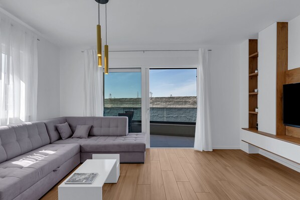 Una sala de estar moderna con un sofá seccional gris, una mesa de centro blanca y un televisor grande sobre una estantería de madera.