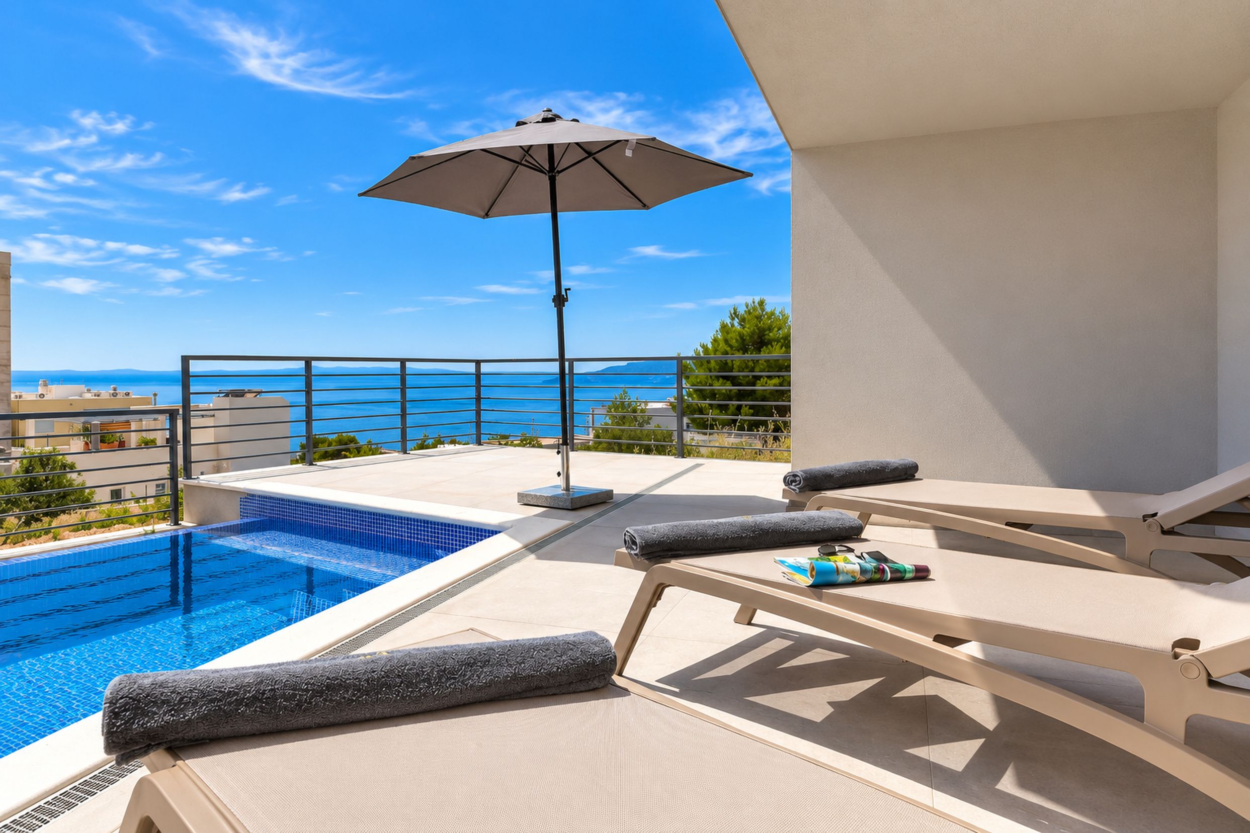 A poolside area with lounge chairs and an umbrella, overlooking a clear blue sea.
