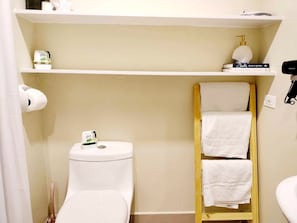 Un baño con inodoro, estante de artículos de aseo y toallero.