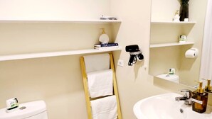 Een badkamer met toilet, wastafel, handdoekhouder en planken met toiletartikelen.