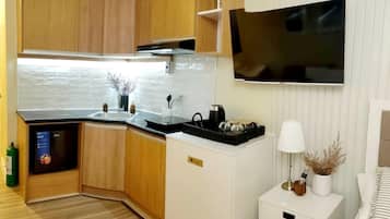 Cozinha compacta com armários de madeira, bancada preta e TV integrada.