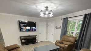 A living room with leather sofas, a coffee table, a TV on the wall, and a ceiling fan. - Brand new home less than one mile to Bryson City! (Bryson City)