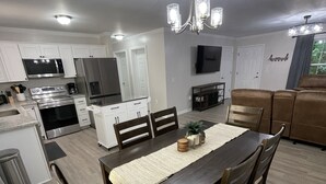A modern kitchen with white cabinets, stainless steel appliances, and a dining area with a wooden table and chairs. - Brand new home less than one mile to Bryson City! (Bryson City)