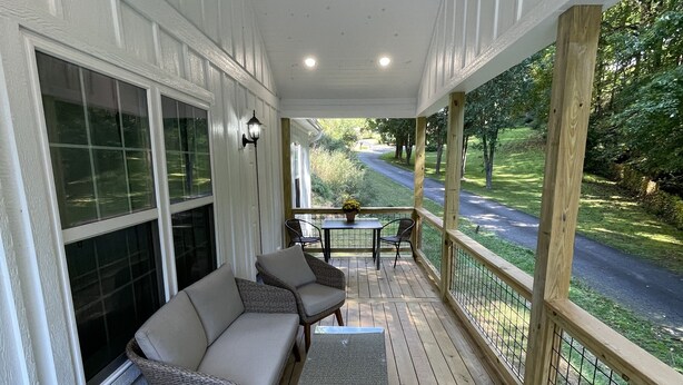 A covered porch with a cushioned seating area, a small table, and a view of a road and greenery. - Brand new home less than one mile to Bryson City! (Bryson City)