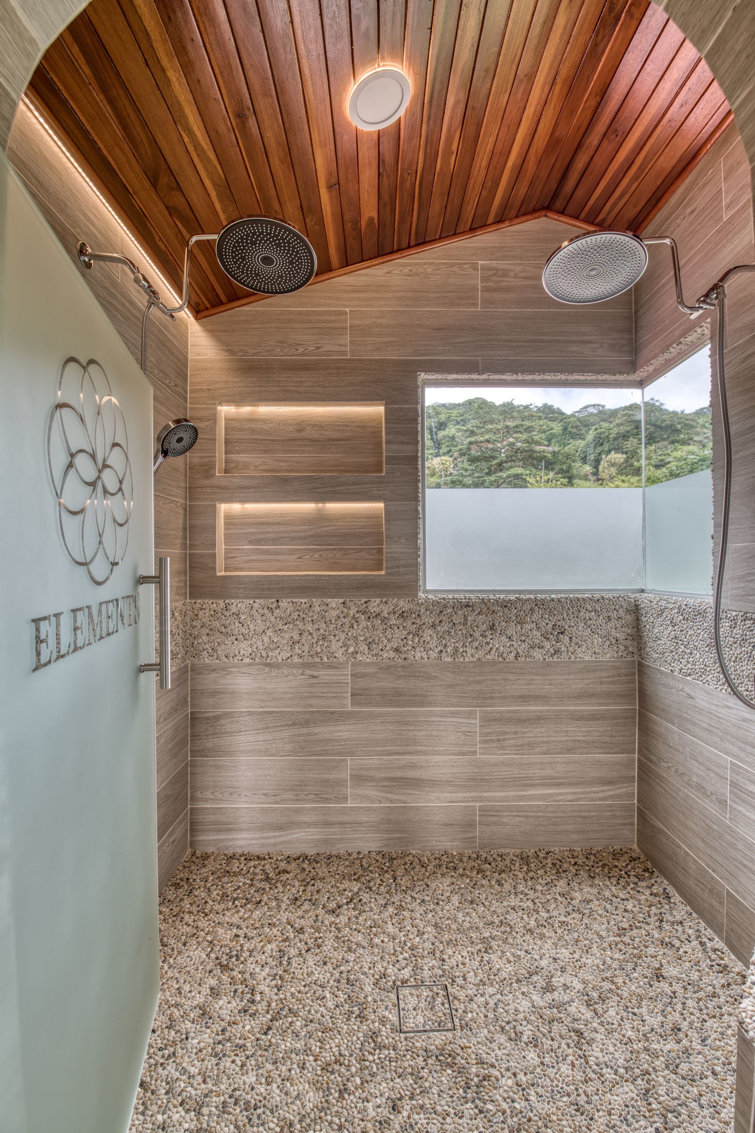 A modern shower area with wooden ceiling and walls, a window with a view, and a decorative wall piece.