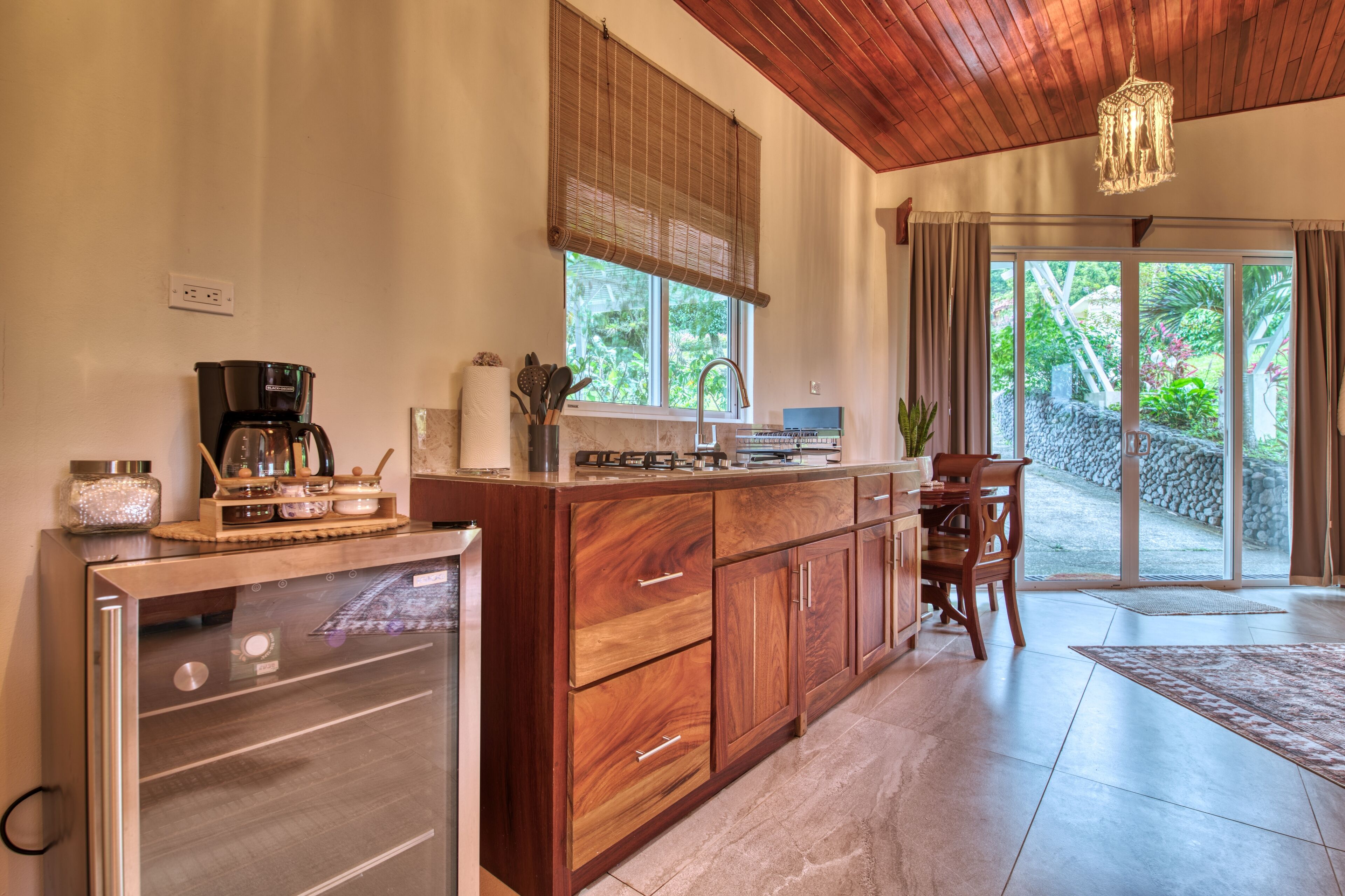 Cocina con armarios de madera, horno empotrado, cafetera y ventana con vistas a un jardín.