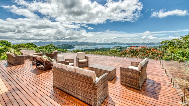 A wooden deck with wicker furniture and a view of a lake and mountains.