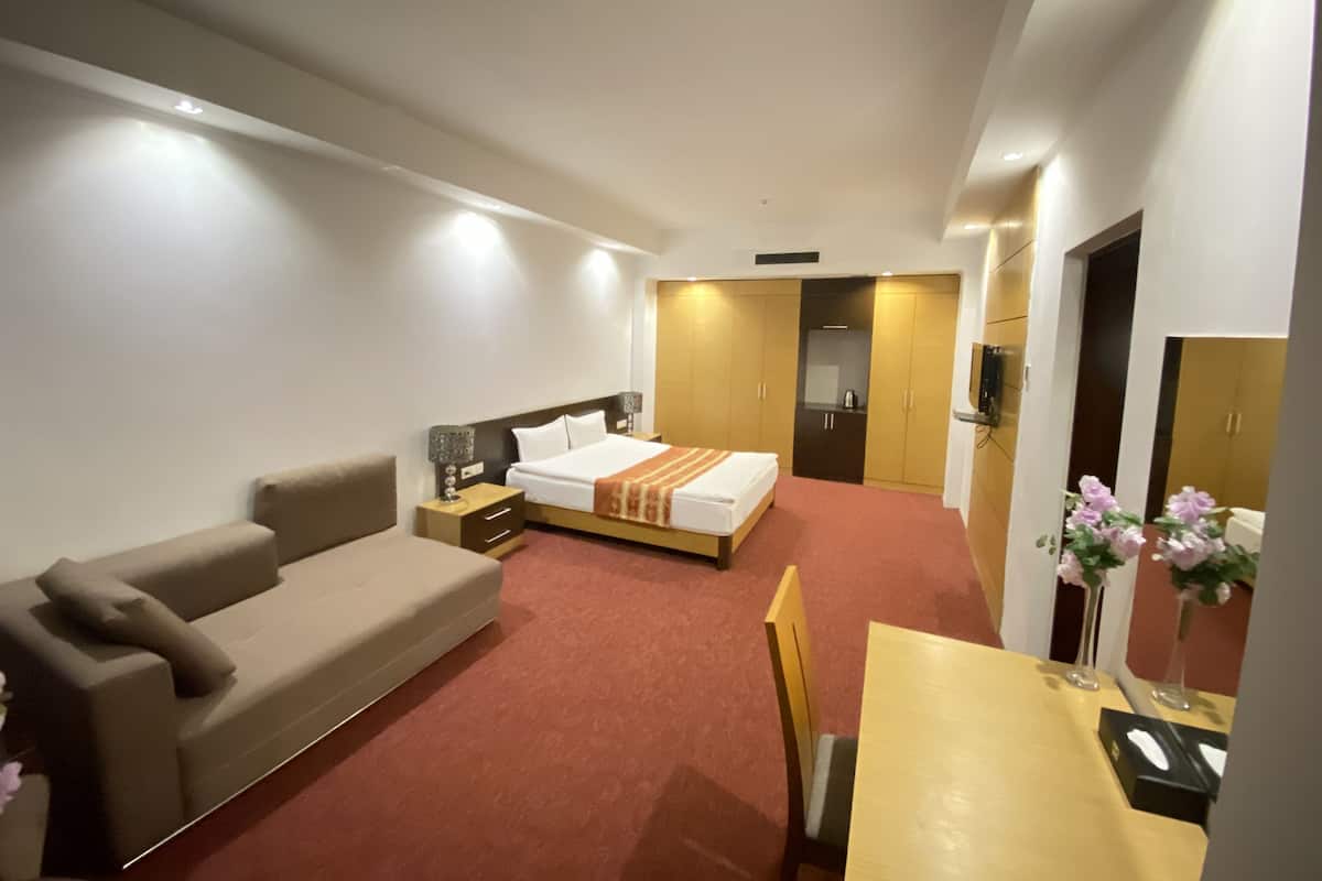 A hotel room with a bed, a sofa, a desk, and a TV.