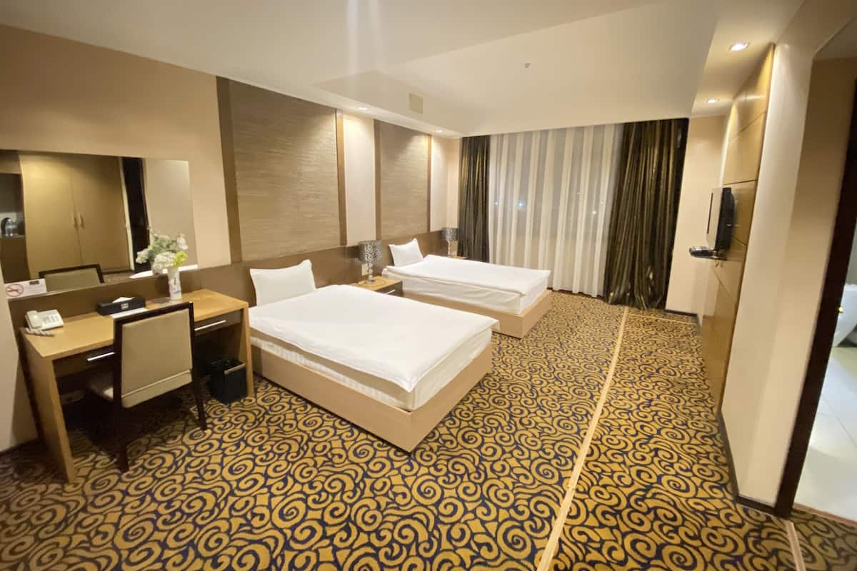 A hotel room with two beds, a desk, a chair, a telephone, a mirror, and a television.