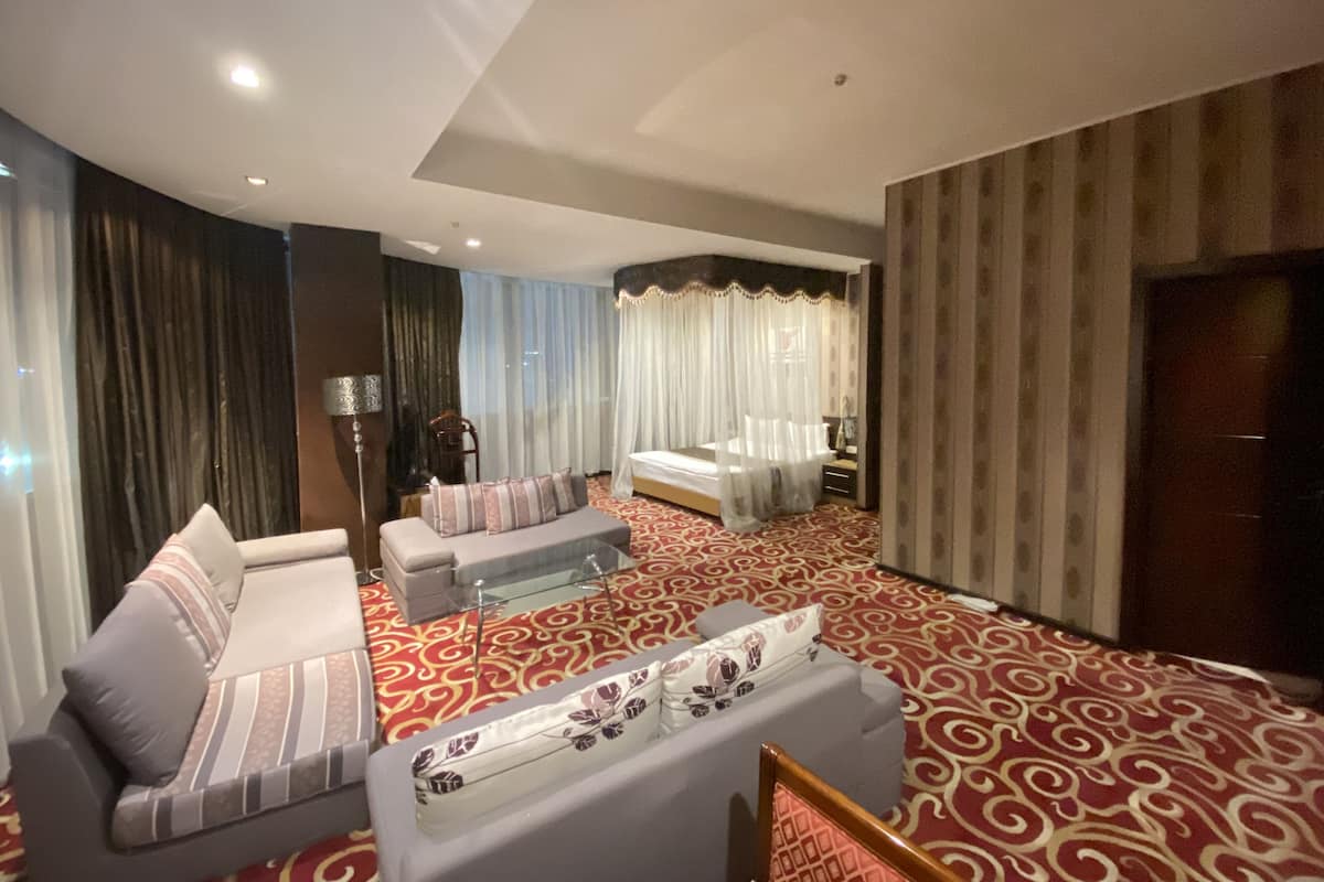 A hotel room with a sofa, a small table, a bed with a canopy, and a patterned carpet.