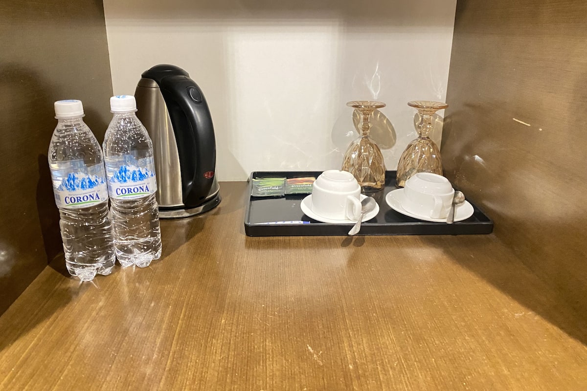 A hotel room with a wooden table featuring a kettle, two bottles of water, a tray with a cup and saucer, and two glass vases.