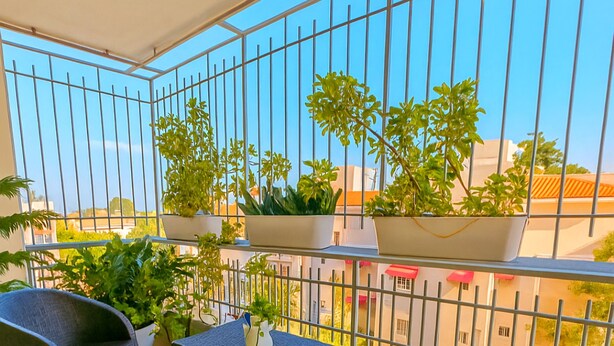Un balcón con muebles de mimbre, plantas en macetas y vistas a edificios.