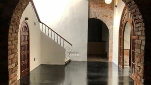 Un intérieur spacieux doté d’un sol en béton poli, d’un escalier avec une rampe en métal et d’arcs en pierre encadrant l’espace.