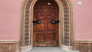 Une porte en bois surmontée d’un arc décoratif, avec une enseigne au-dessus et un numéro sur le mur.