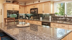 Una cocina con encimeras de granito, gabinetes de madera, horno empotrado, microondas y una isla grande con taburetes de bar.