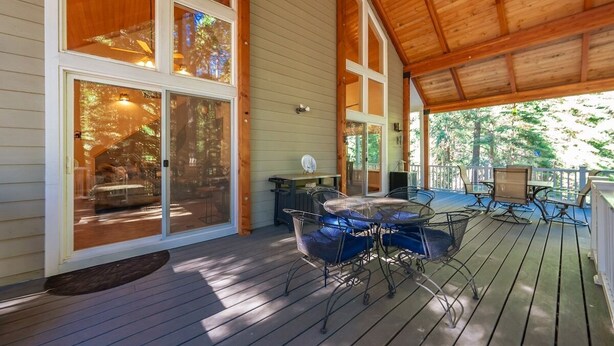 Una terraza techada con zona de comedor, amplias ventanas y vistas a los árboles circundantes.
