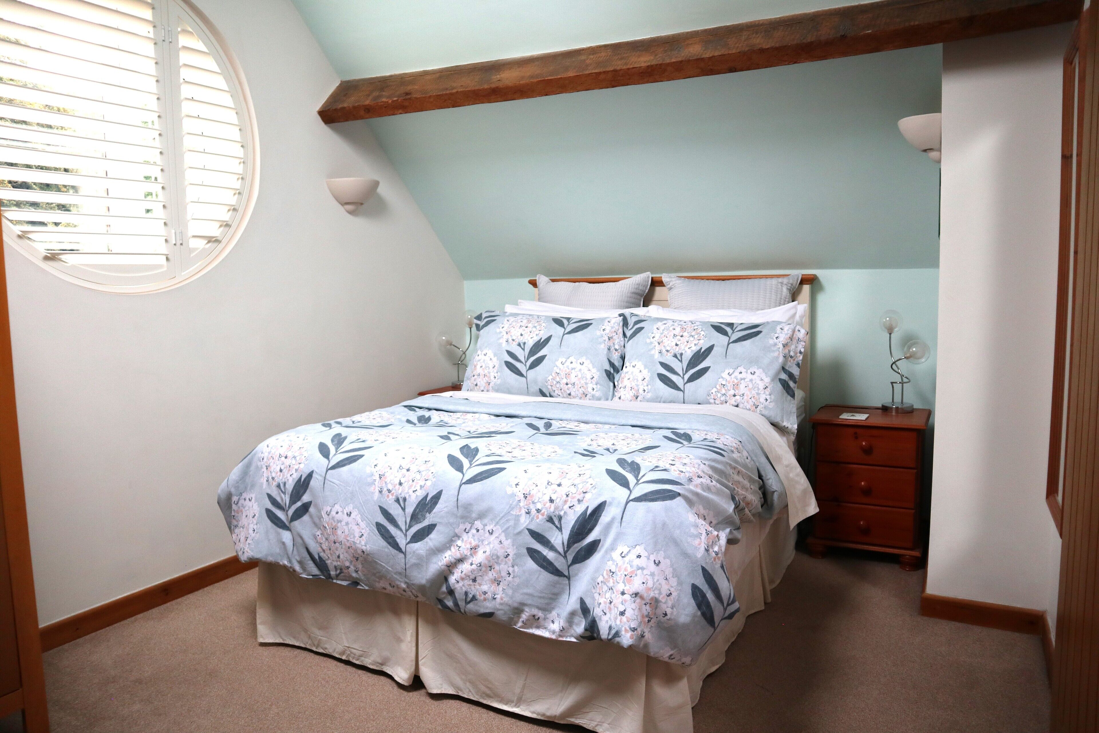 A bedroom with a bed, a nightstand, a dresser, a window with blinds, and a sloped ceiling.