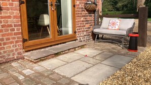 A brick building with a glass door, a wicker sofa with a cushion, and a statue of an owl. - Charming 2-bed Cottage, Beautiful Views, Knutsford (Knutsford)